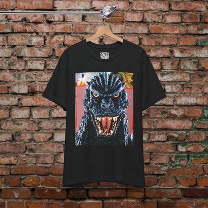 A black t-shirt with a graphic of a large, menacing-looking monster with a fierce expression and open mouth, hanging on a wooden hanger against a brick wall.